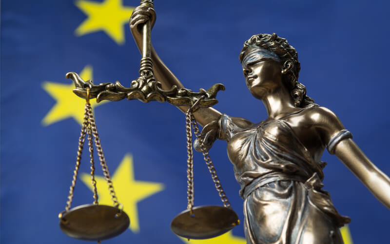 statue of Blind Justice with scales with European Union flag in the background